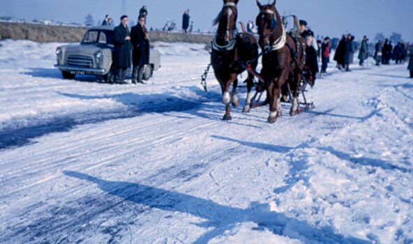 Foto uit 1963 met daarop paarden met een arrenslee op het ijs in Kinderdijk. Ze zijn omringt door veel mensen op het ijs en staat zelfs een auto op het ijs.